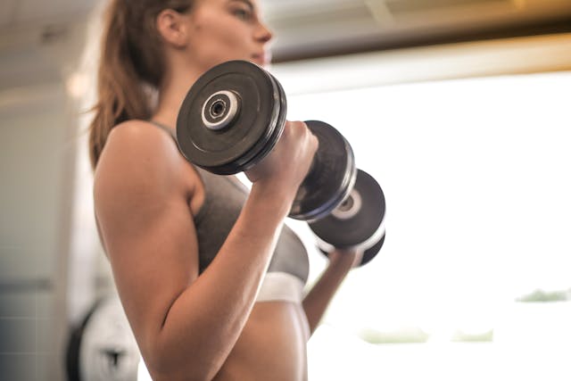 Woman in gray sports bra holding black dumbbell Woman in gray sports bra holding black dumbbell