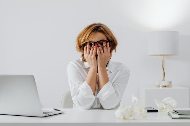 Woman sitting on a desk covering her eyes with her hands Woman sitting on a desk covering her eyes with her hands