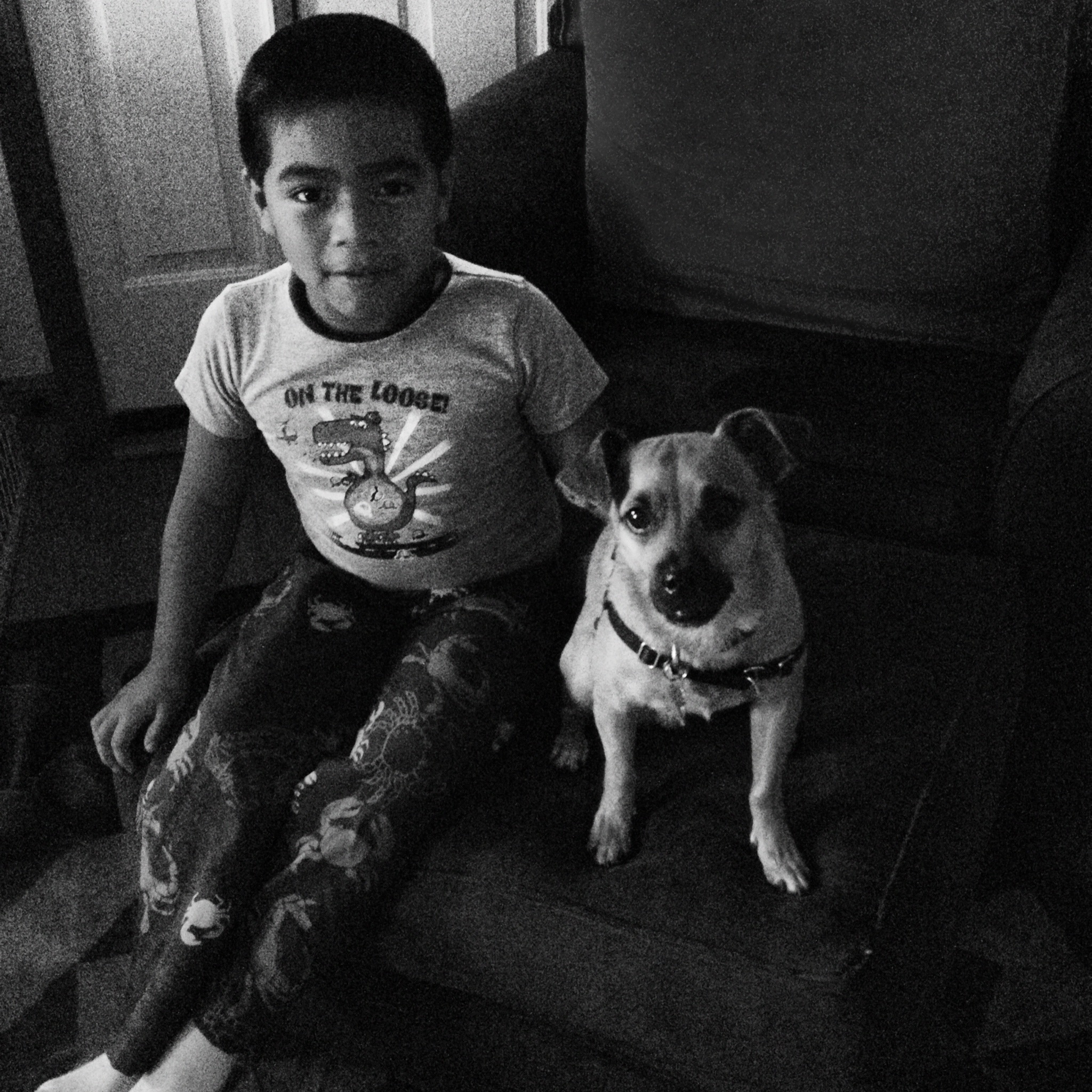 Black & White photo of an elementary aged boy sitting on a couch next to a small chihuahua mix dog.