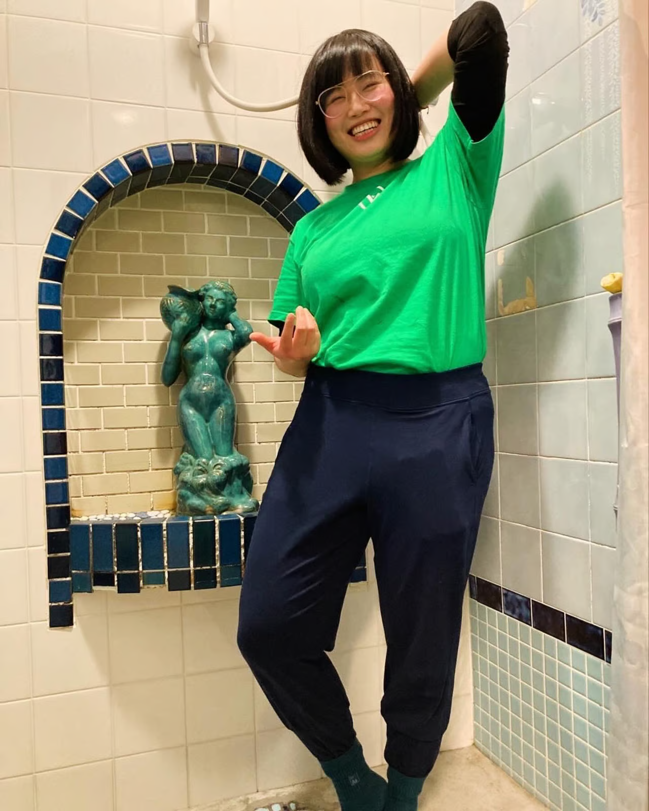 Smiling woman in a green Venus Weightlifting shirt posing playfully in front of a decorative tiled wall with a small fountain Smiling woman in a green Venus Weightlifting shirt posing playfully in front of a decorative tiled wall with a small fountain
