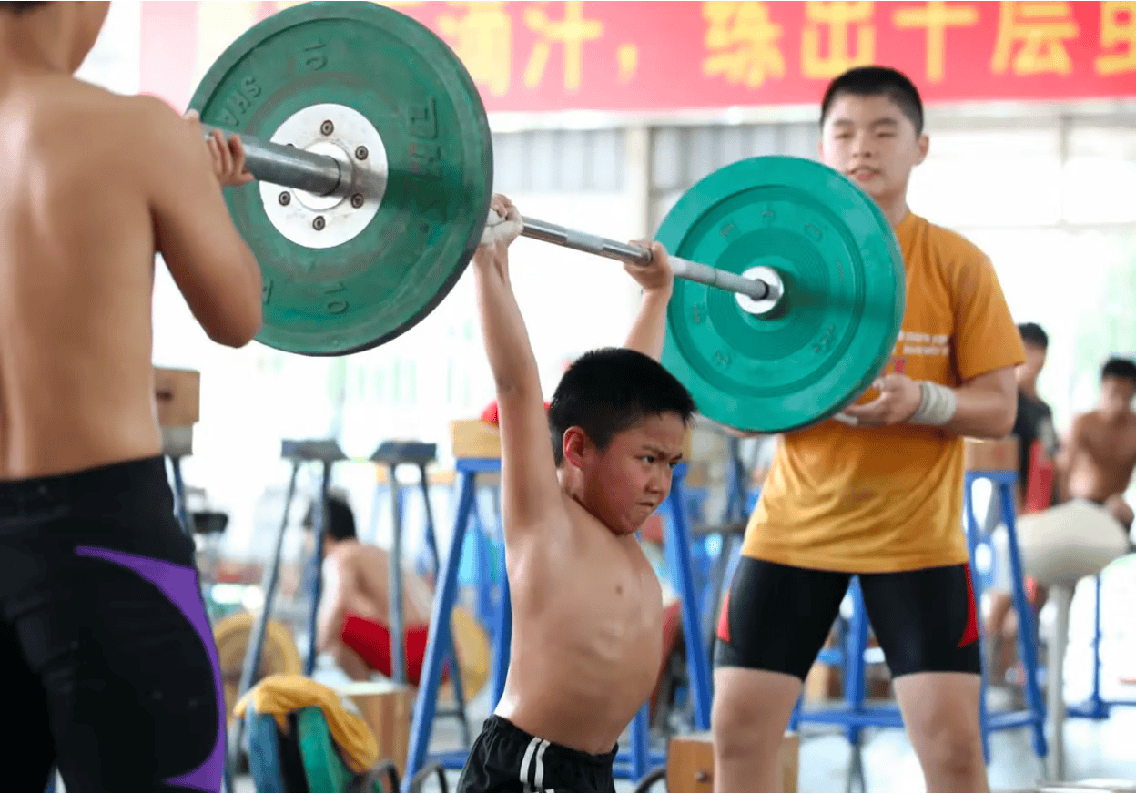 Young Chinese weightlifter training with a barbell in an Olympic weightlifting gym, showcasing early strength development. Young Chinese weightlifter training with a barbell in an Olympic weightlifting gym, showcasing early strength development.