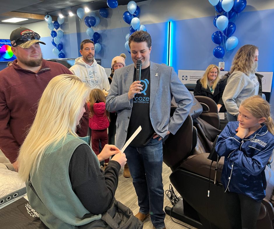 Nico Marasco, co-owner of Snooze Mattress Co., in Omaha, NE, watches as a woman opens an envelope with a prize in it at the grand opening celebration on Feb. 20.