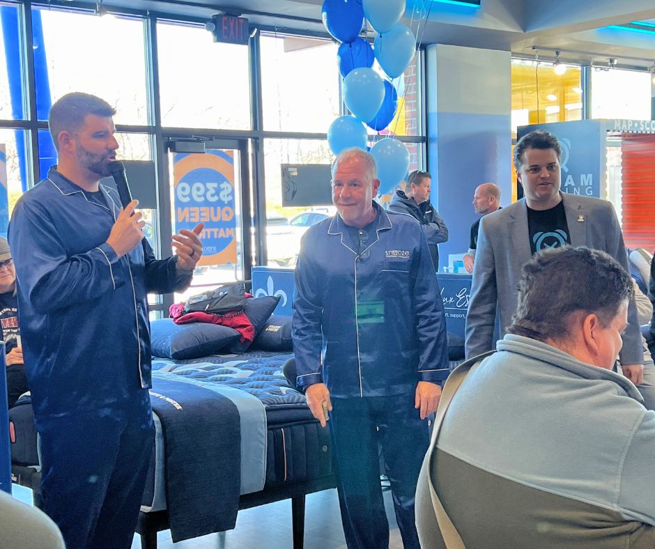 Nico Marasco, co-owner of Snooze Mattress Co., in Omaha, NE, watches as a woman opens an envelope with a prize in it at the grand opening celebration on Feb. 20.