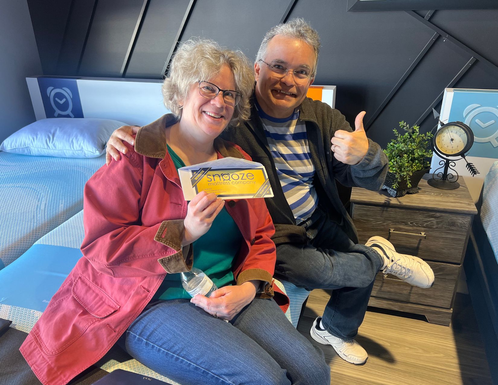 A couple show off a golden ticket for a $5 premium Sealy mattress at the Parker, CO Snooze Mattress Co. grand opening event. 