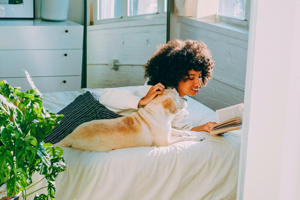 woman on bed reading with dog