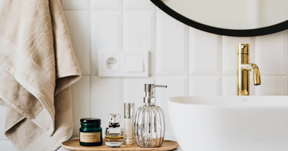 Close-up of a bathroom counter with neatly arranged skincare products, including a jar, serum bottles, and a soap dispenser, next to a white sink and gold faucet, highlighting the essentials of a personalized skincare routine.