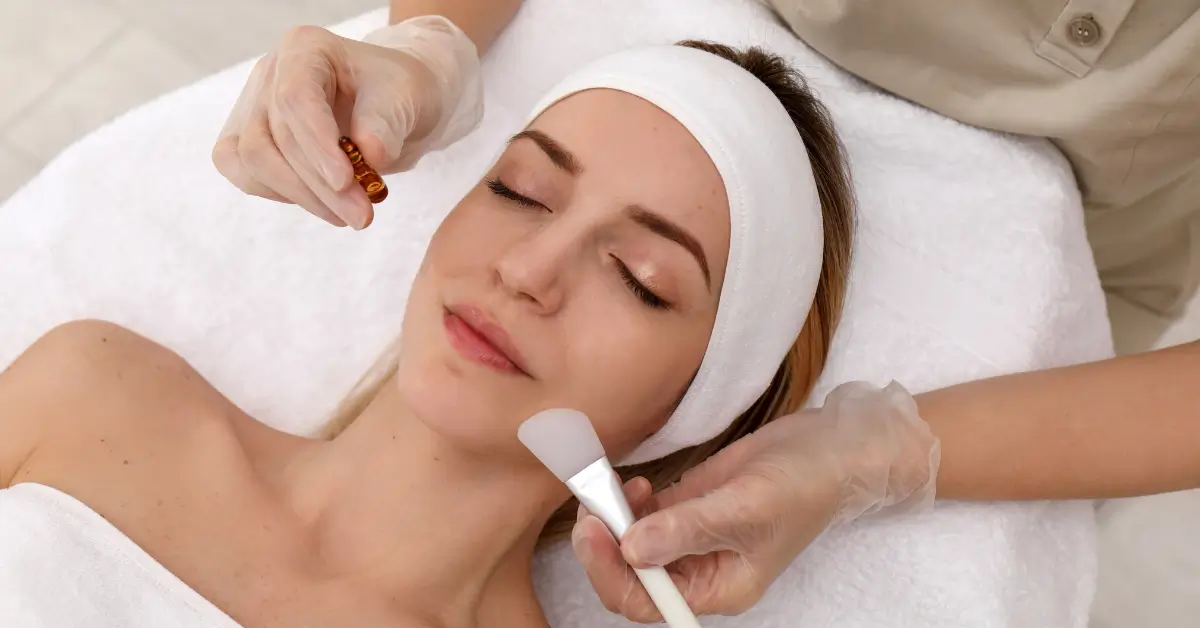 Client receiving a professional facial treatment from an aesthetician applying serum and using a brush