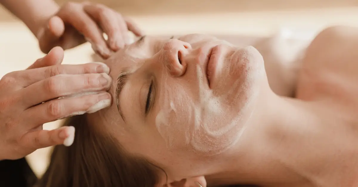Woman relaxing with eyes closed during a traditional facial treatment as an aesthetician massages a foaming cleanser onto her skin Woman relaxing with eyes closed during a traditional facial treatment as an aesthetician massages a foaming cleanser onto her skin