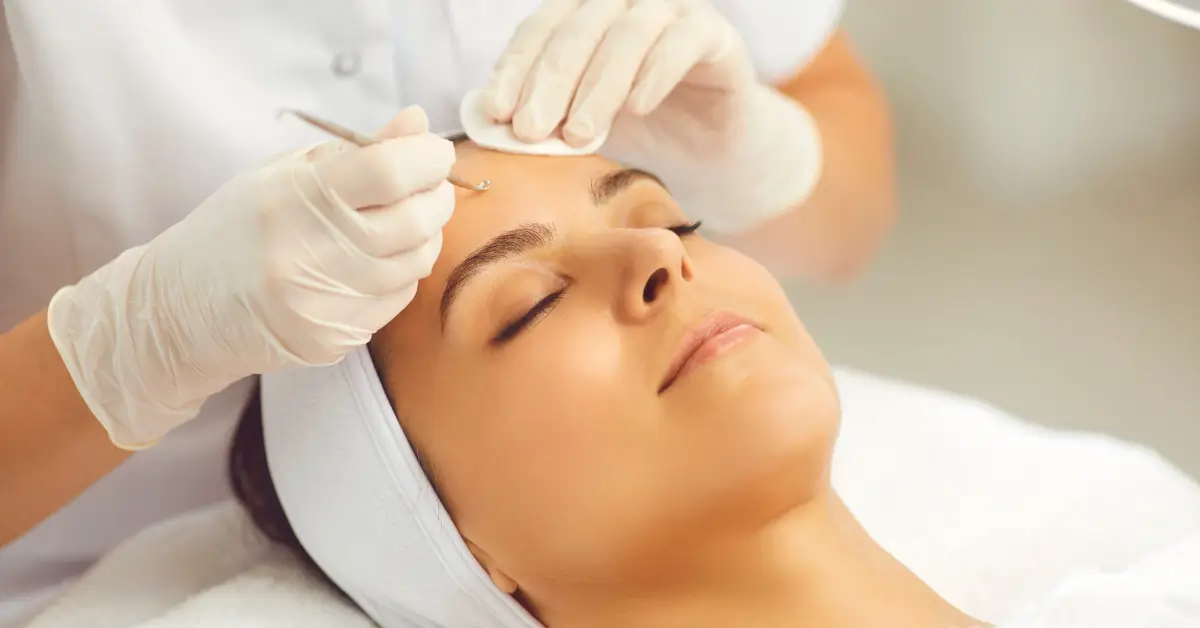 Woman with eyes closed receiving a traditional facial treatment as an aesthetician uses an extraction tool on her forehead Woman with eyes closed receiving a traditional facial treatment as an aesthetician uses an extraction tool on her forehead
