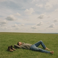 Man lying in open meadow gazing at wide sky, boots off and hands behind head in quiet solitude. Man lying in open meadow gazing at wide sky, boots off and hands behind head in quiet solitude.