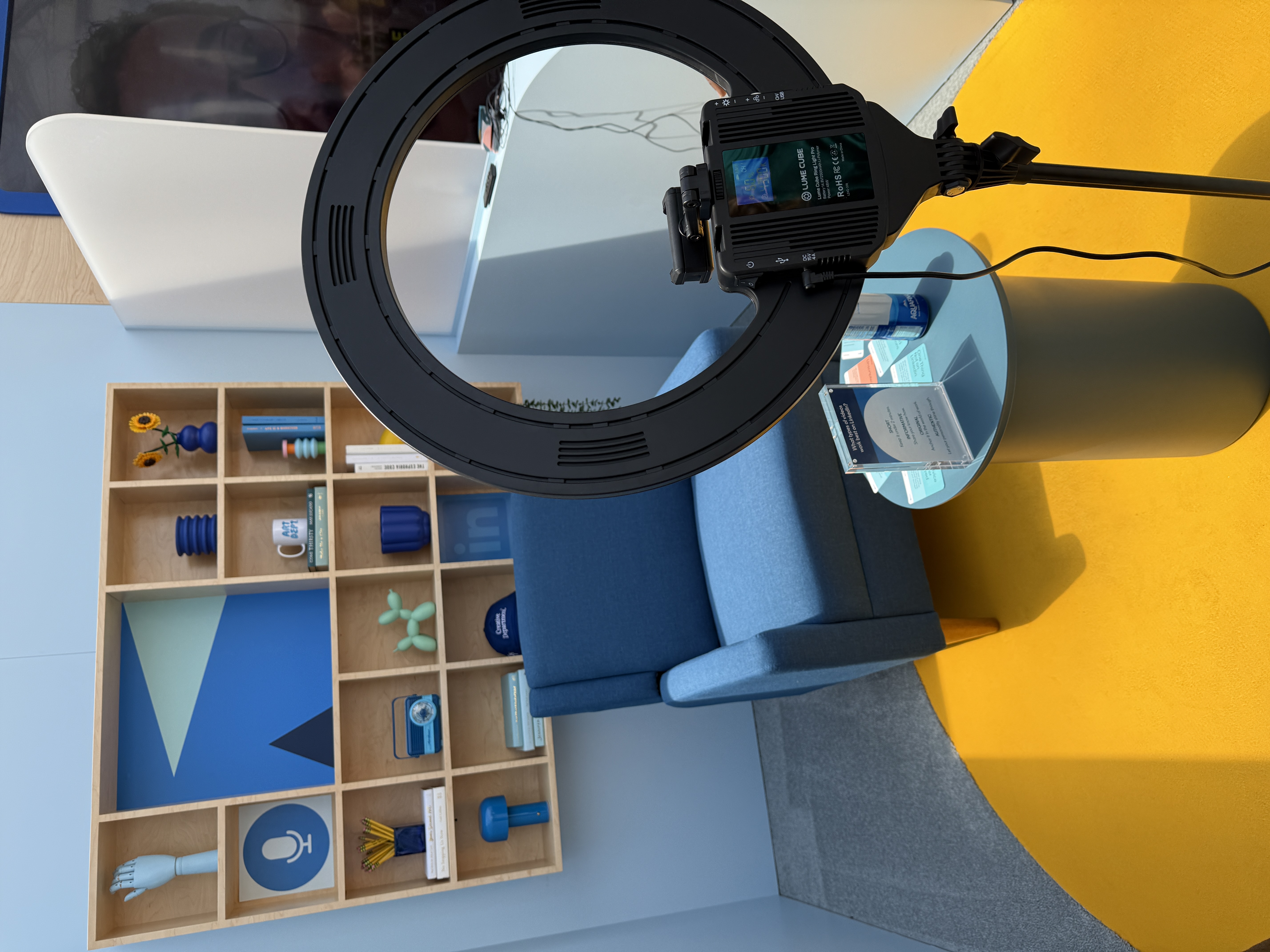 LinkedIn’s on-site video studio at Canva Create featuring a blue armchair, a yellow circular rug, a ring light setup, and a modern shelving display with props and books.