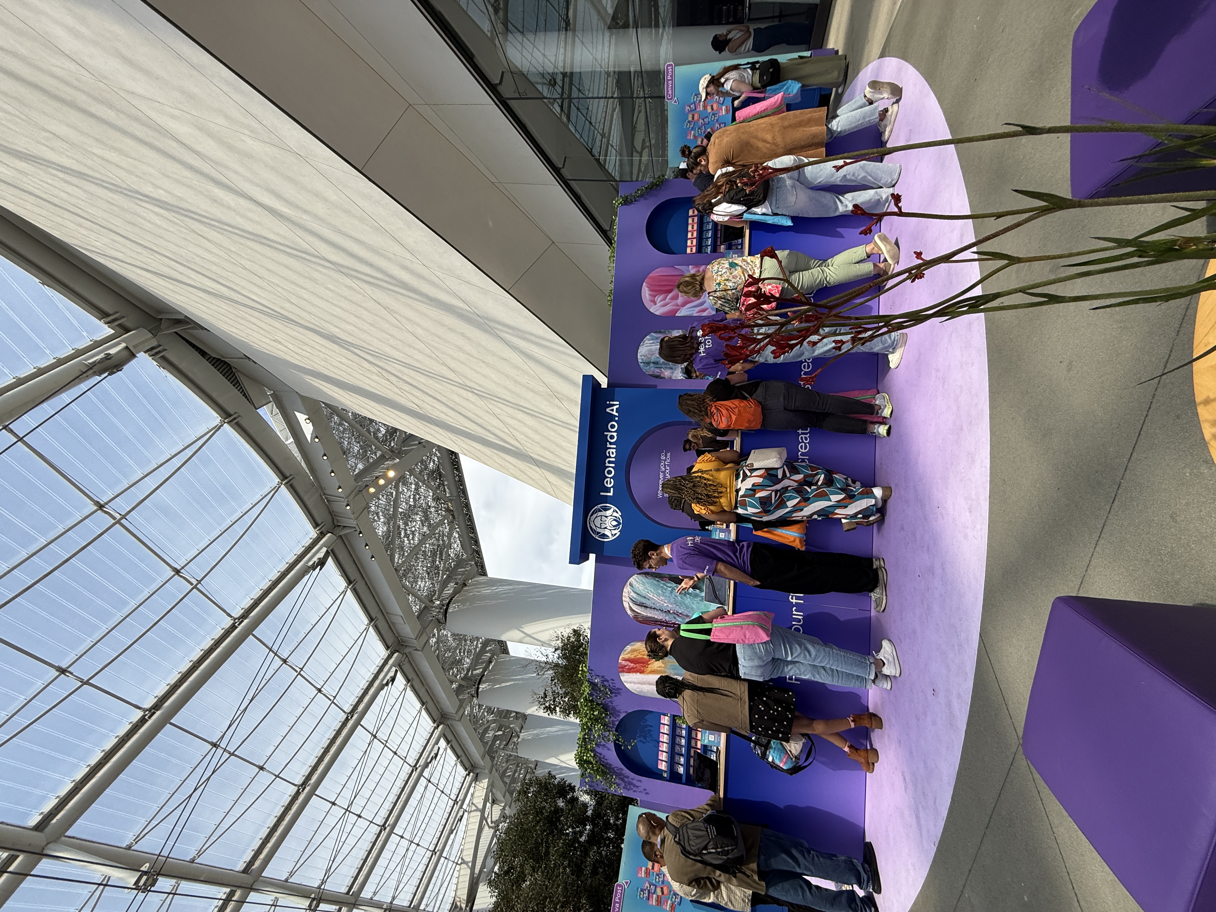 Attendees gathered at the Leonardo.Ai booth during Canva Create, exploring interactive AI image-generation demos at purple counters under a glass-roofed venue.
