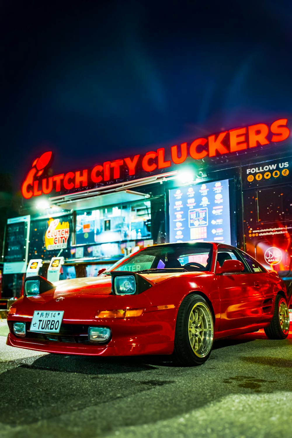 Red sports car parked under Clutch City Cluckers sign after premium ceramic coating in Houston