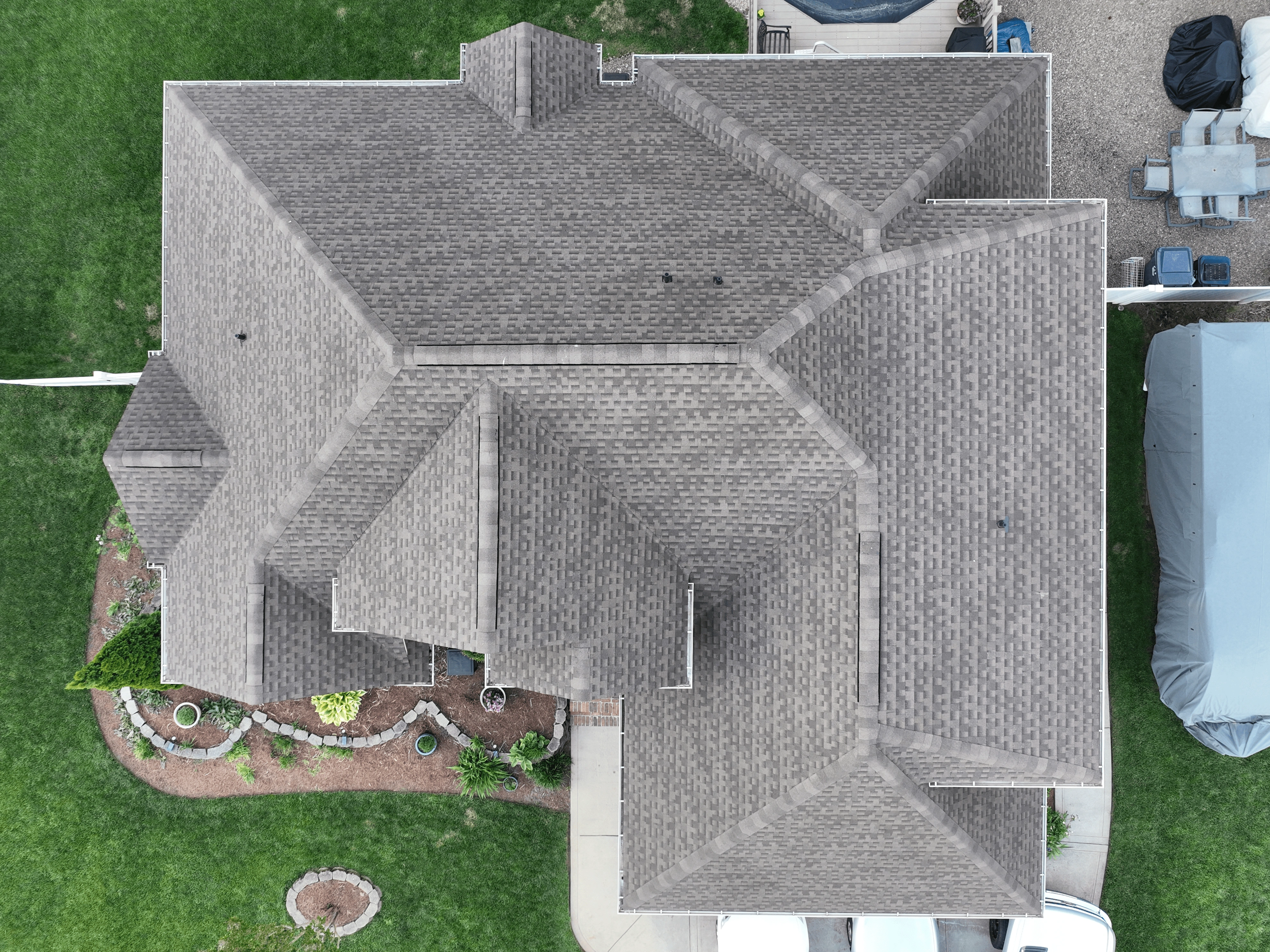 Aerial view of a house featuring a well-maintained roofing system with multiple gabled sections, surrounded by a lush green lawn and a landscaped garden area.