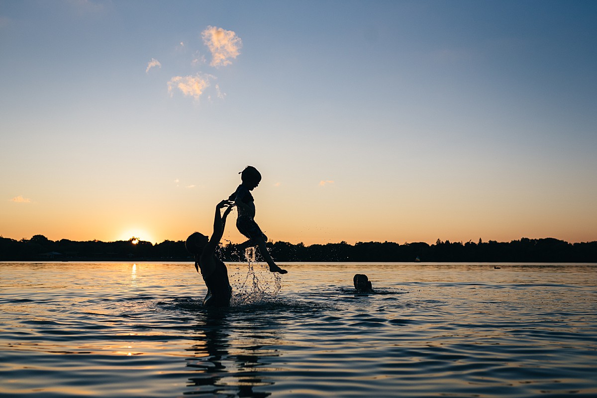 Adult hoists child into the air in a lake during sunset. Silhouette.