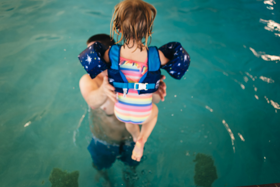 Perspective from above.  A young girl wearing water wings jumping into a pool. Photography phone tips