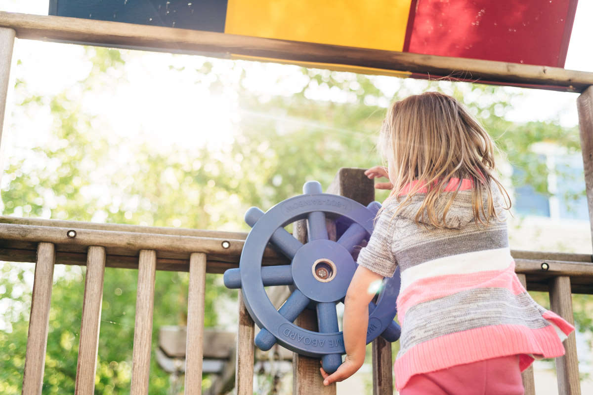 Woodbury family videography session. Little girl spins wheel on playground.