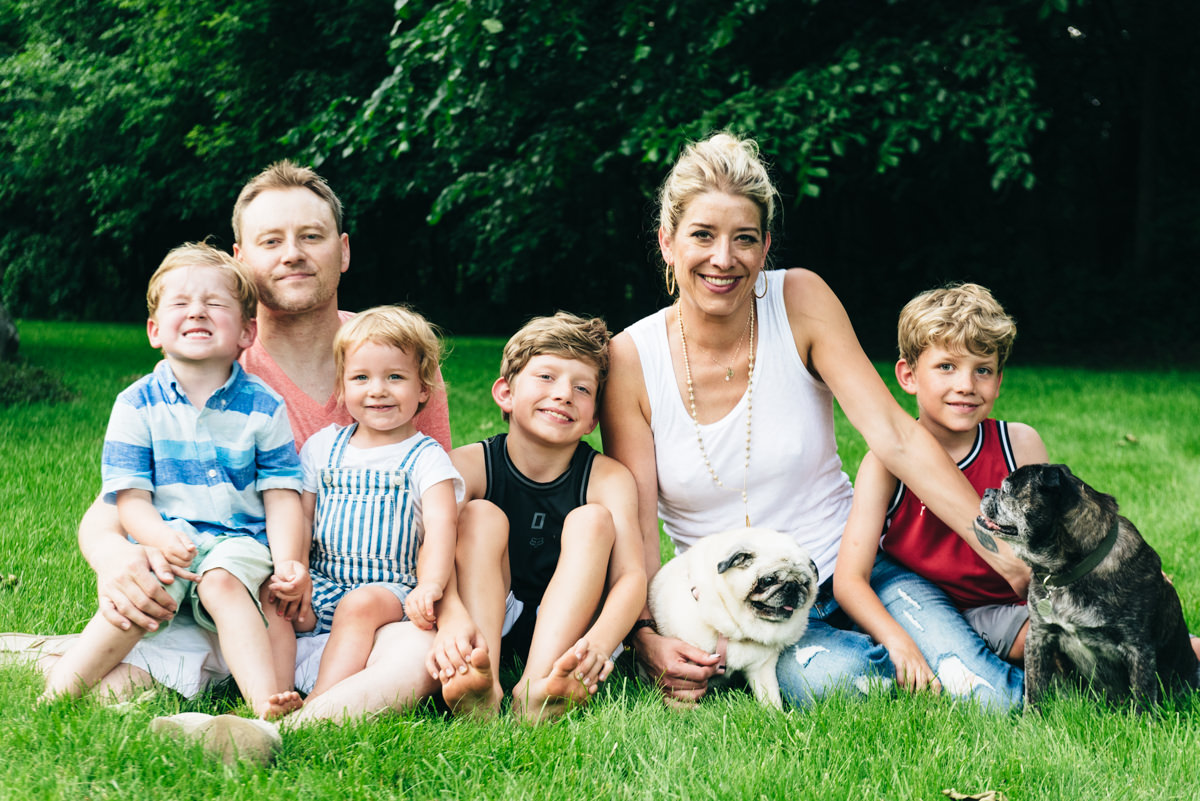 Family of six sits on a blanket in the yard and smiles at camera.