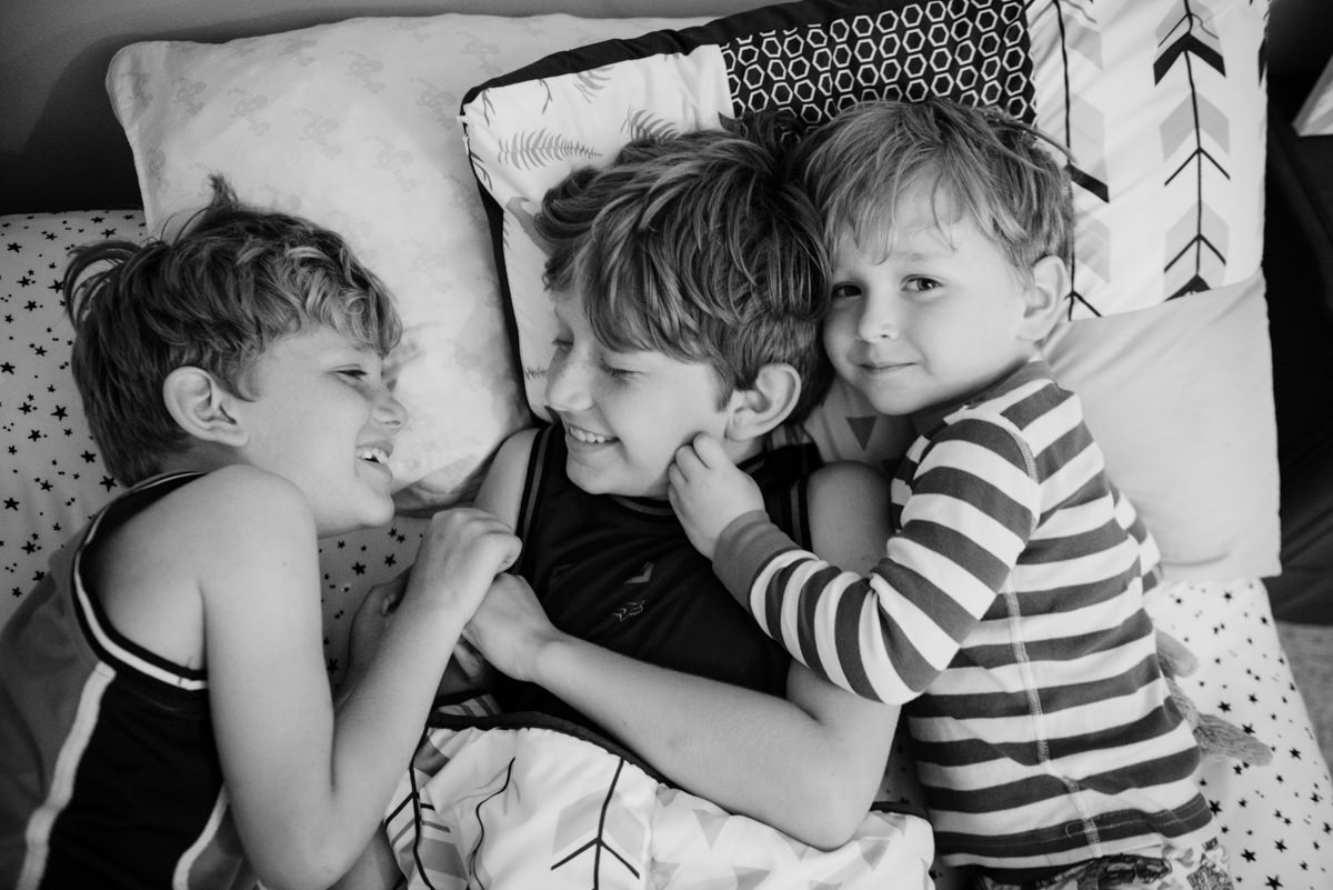 Three kids snuggle in bed and laugh. 