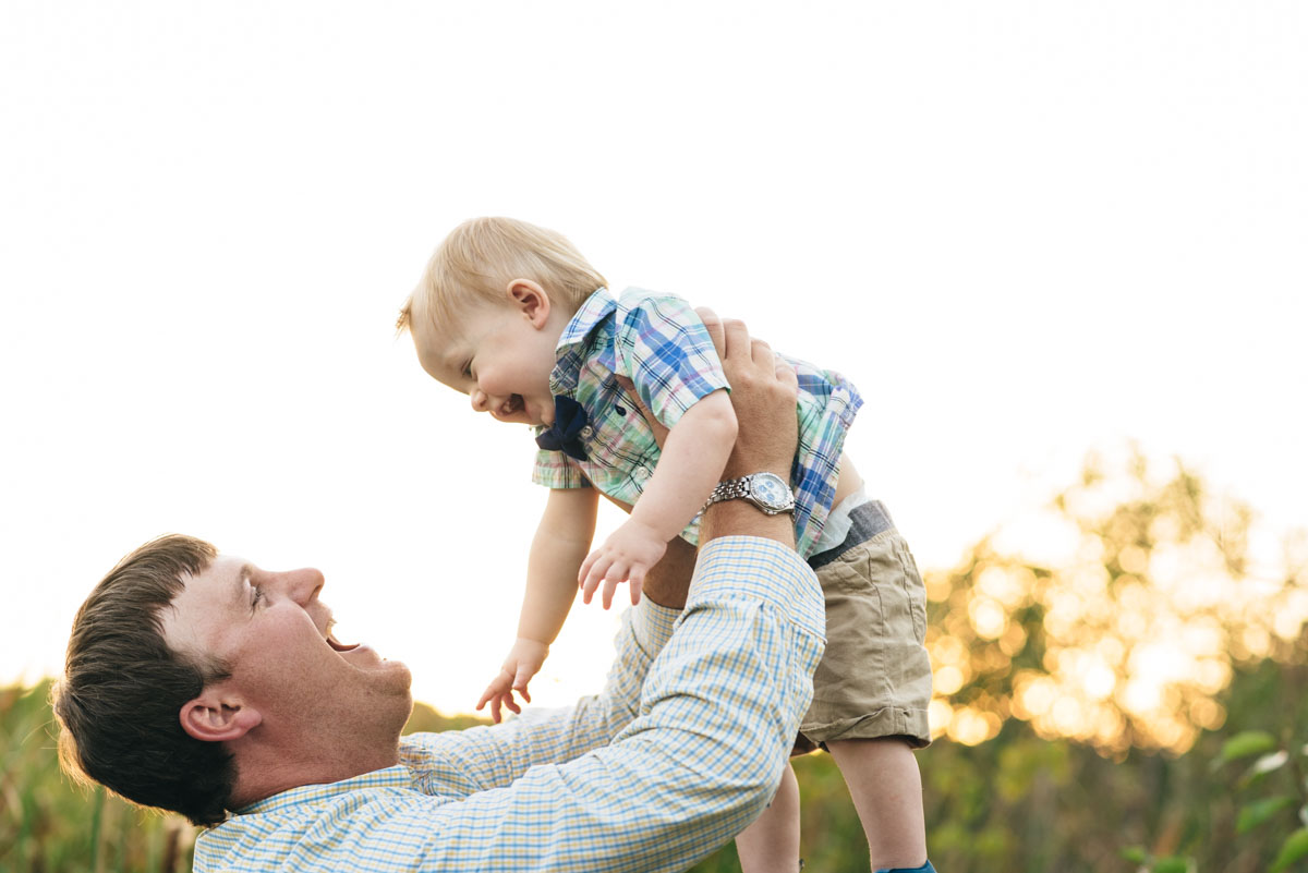 Father holds son up in the air and laughs with him during sunset session.