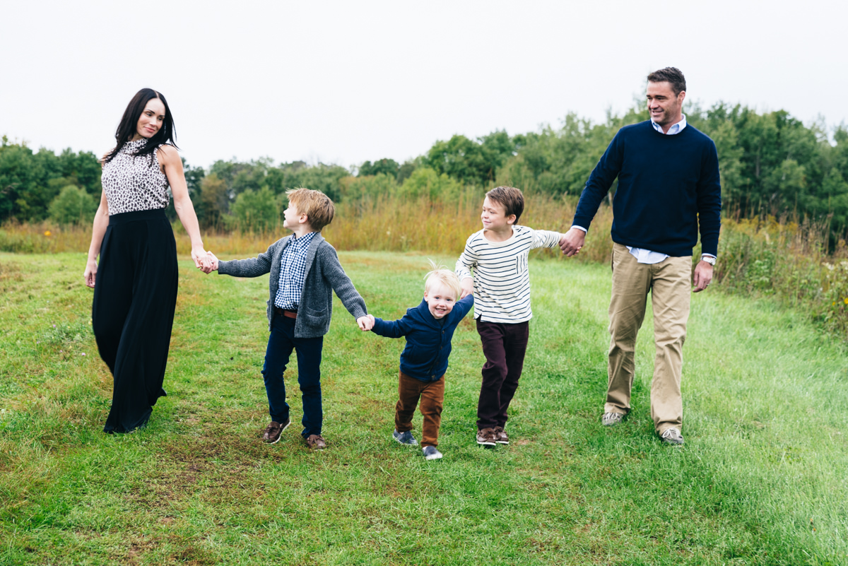 Family of five holds hands and walks to camera with coordinating clothing for family photos.