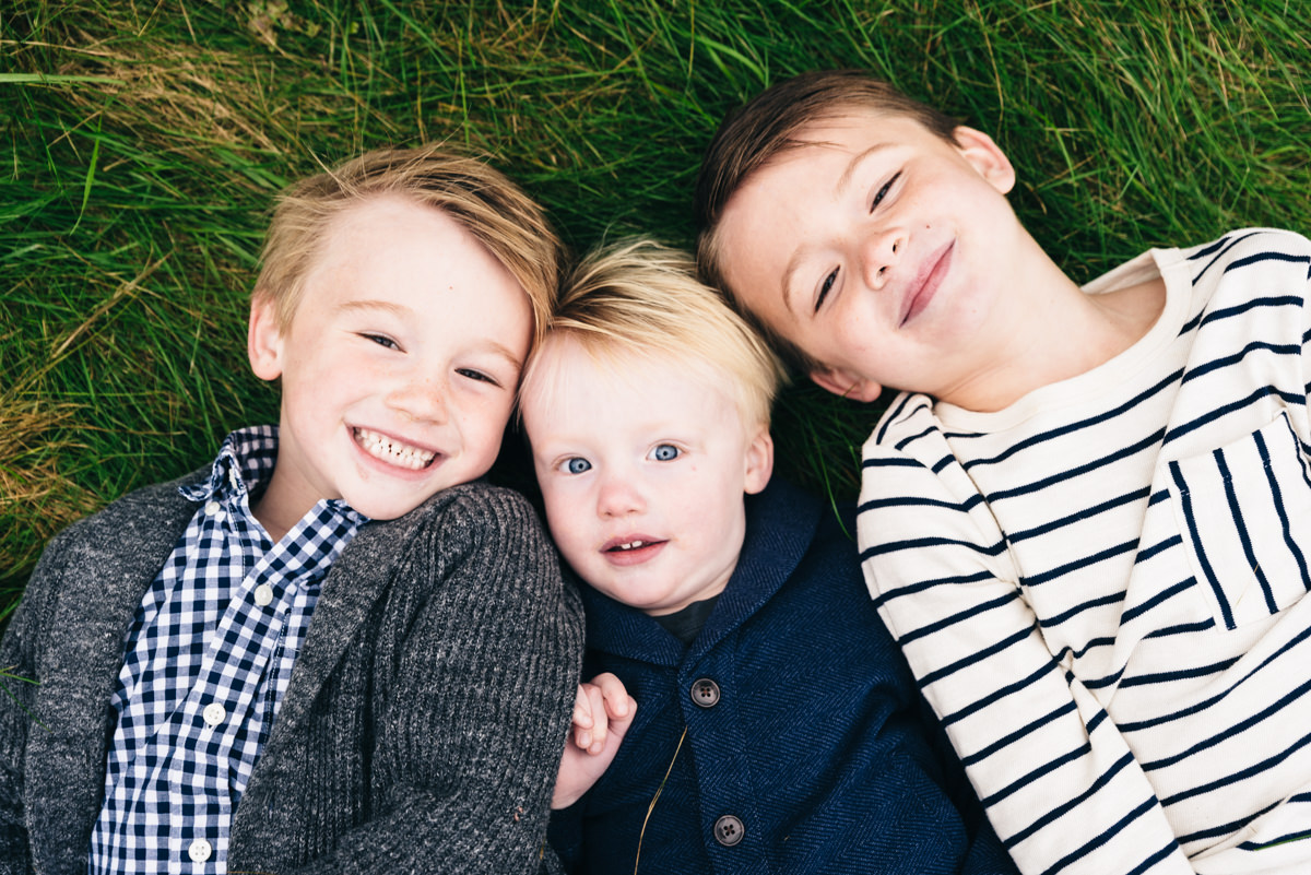 Three boys lay on the grass next to each other looking up at camera.