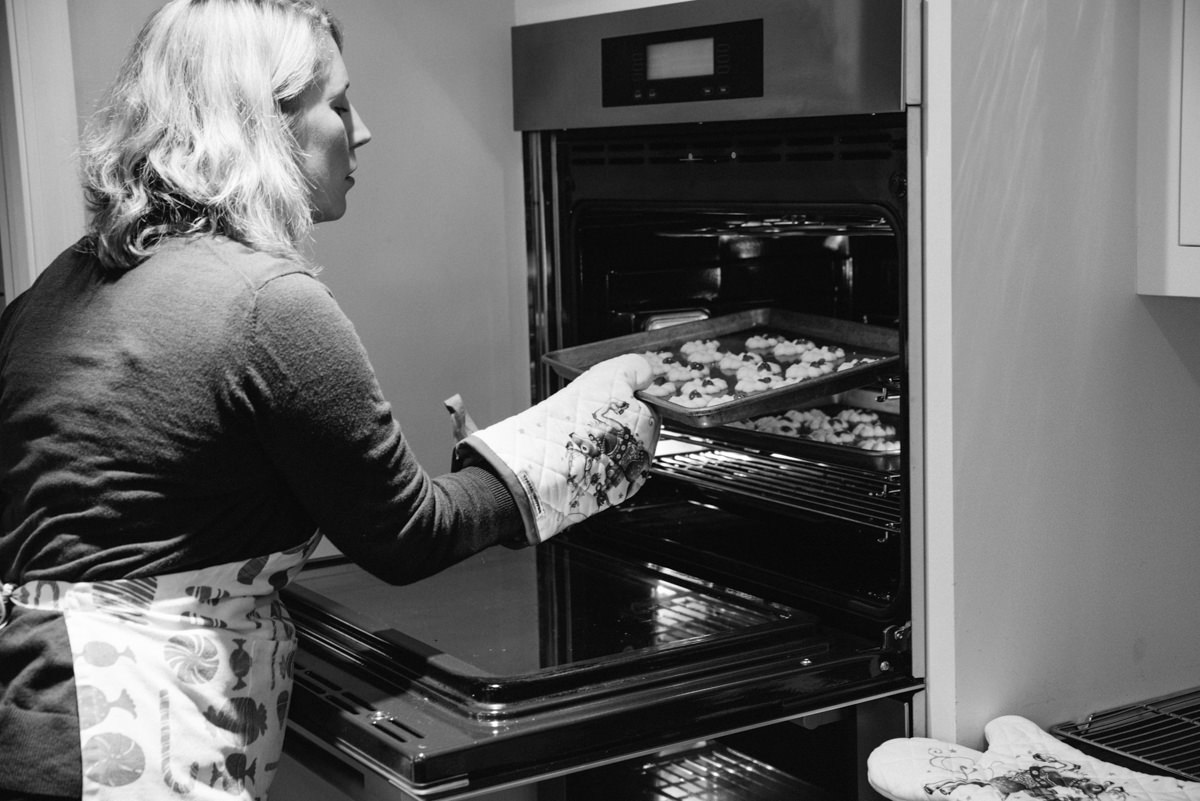 Holiday lifestyle photograph of women putting cookies in the oven.