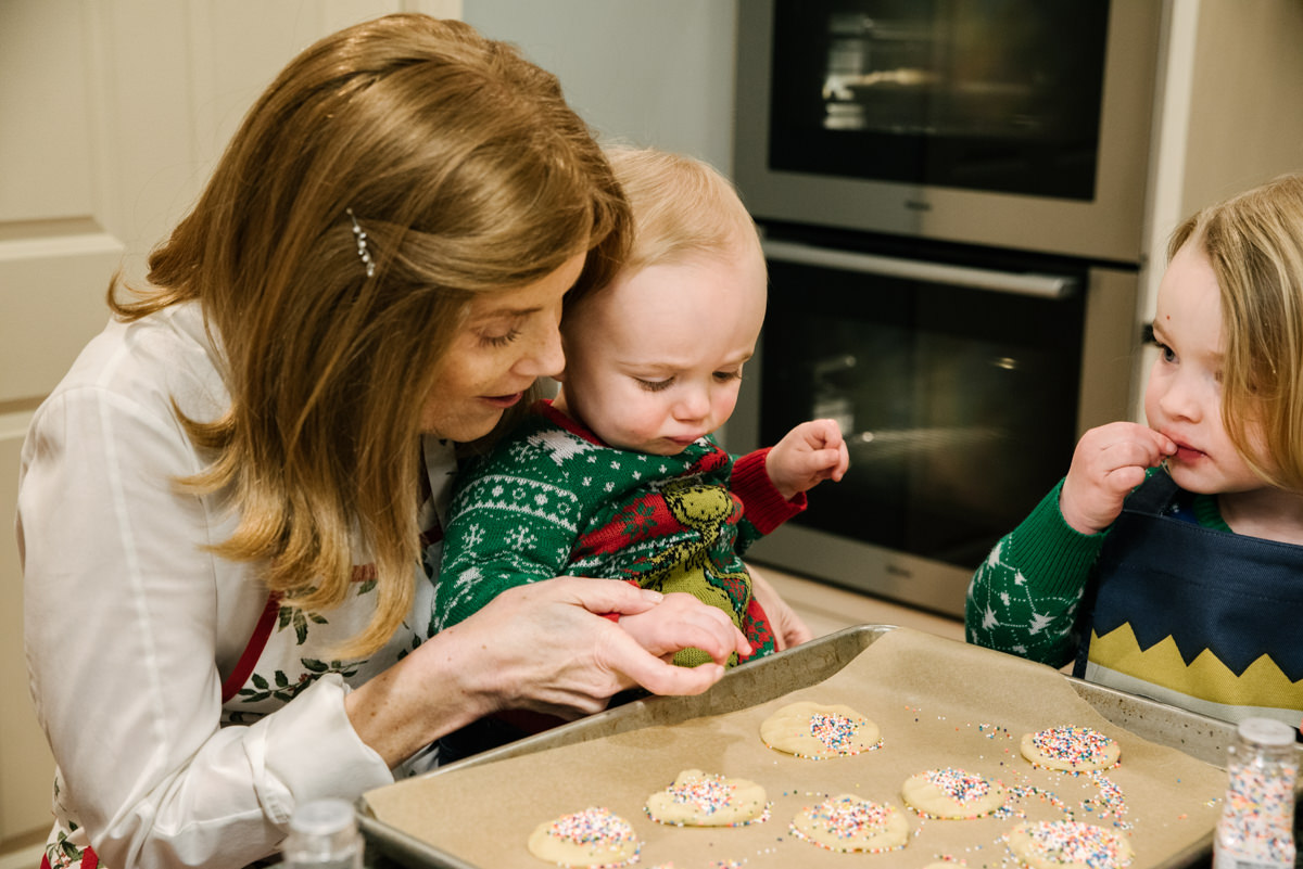 Grandmother helps grandson put sprinkles on holiday cookies during videography session.