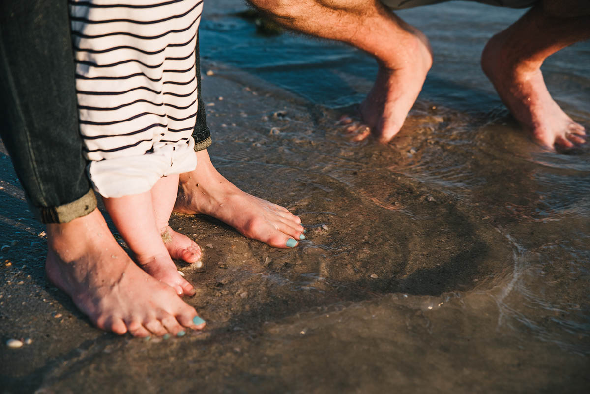 Feel of parents and baby in ocean. Traveling family photographer.