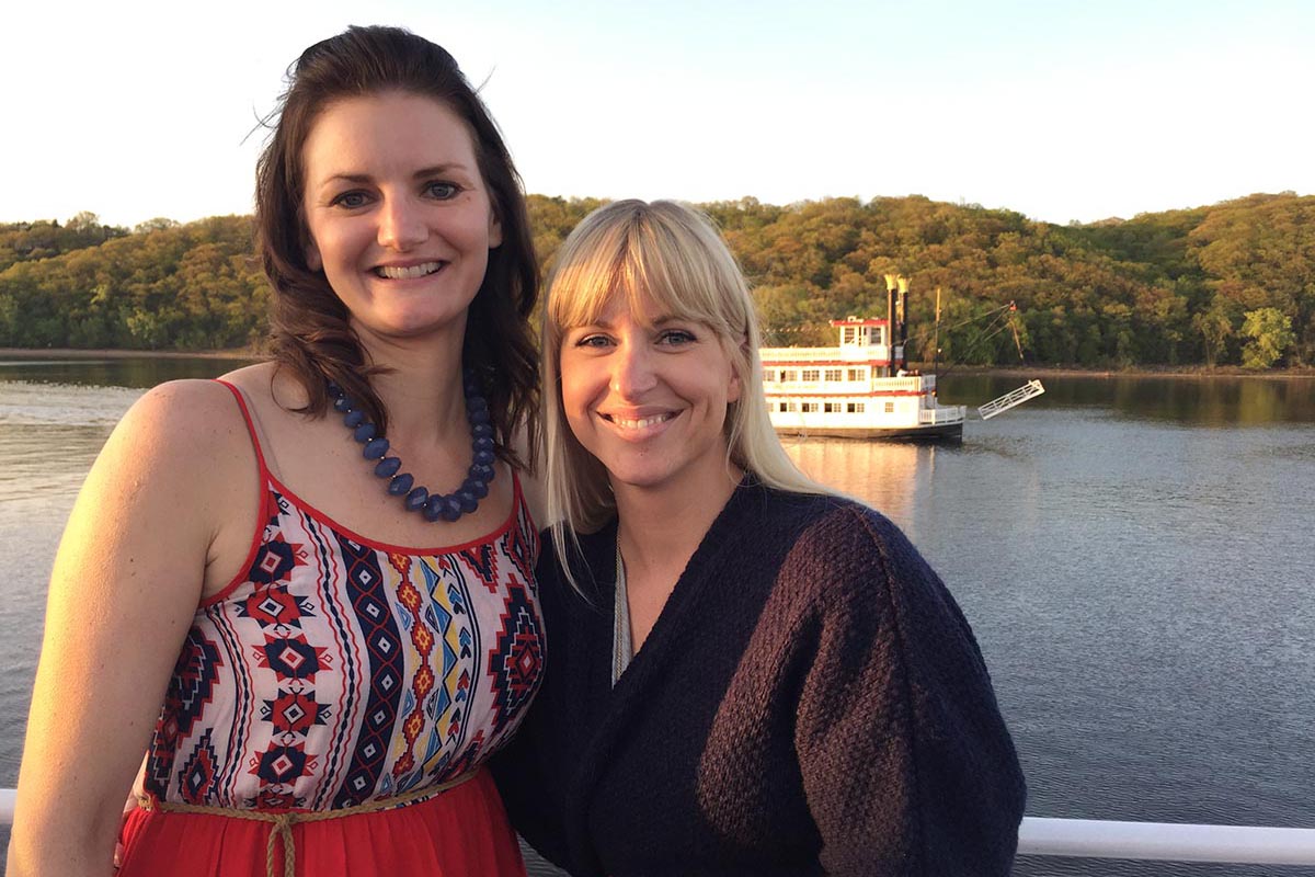 Two women on a dinner cruise boat posing for a photo by the raililng.