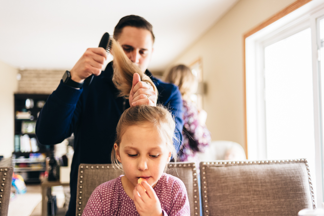 Dad brushing daughters hair at kitchen table.