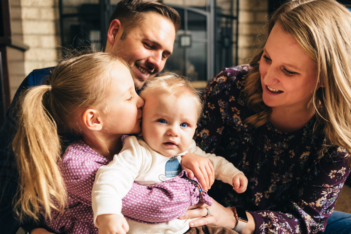 Sister kissing baby brother while mom and dad look on.