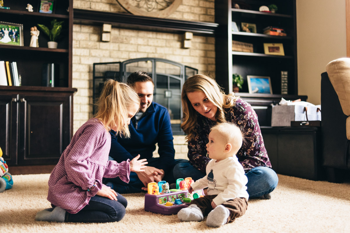 Family of four plays with baby toy in the living room.