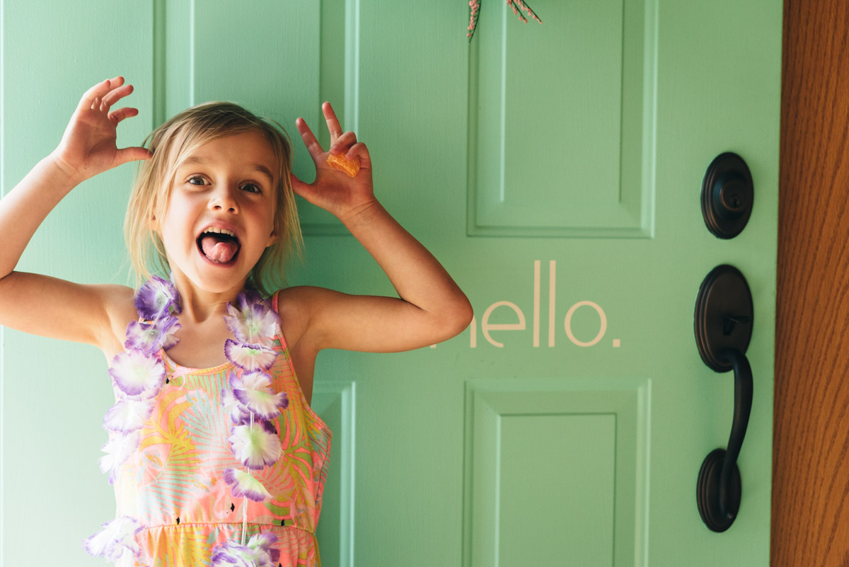 Little girl stands by green door with the word "hello" printed on it.