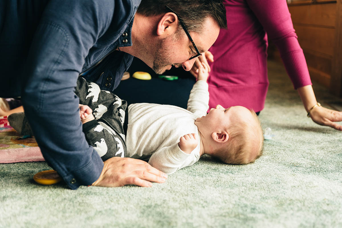 Father hovers over baby son and smiles and plays.