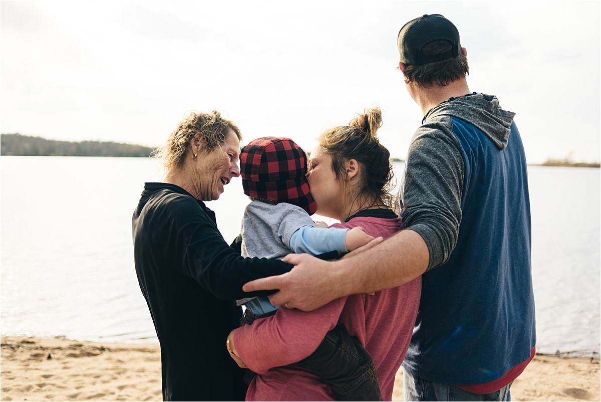 Family of four stands near water and looks out at water.