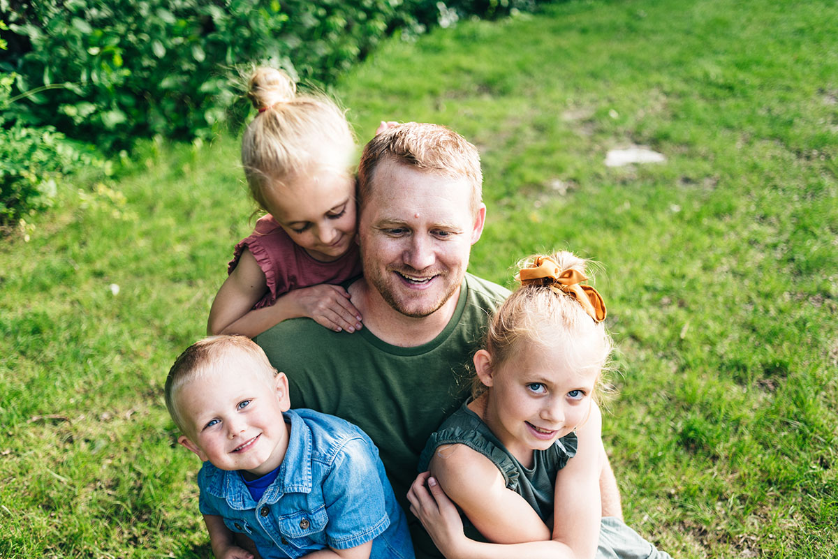 Father sitting with his three children in the grass during family video in Minnesota.