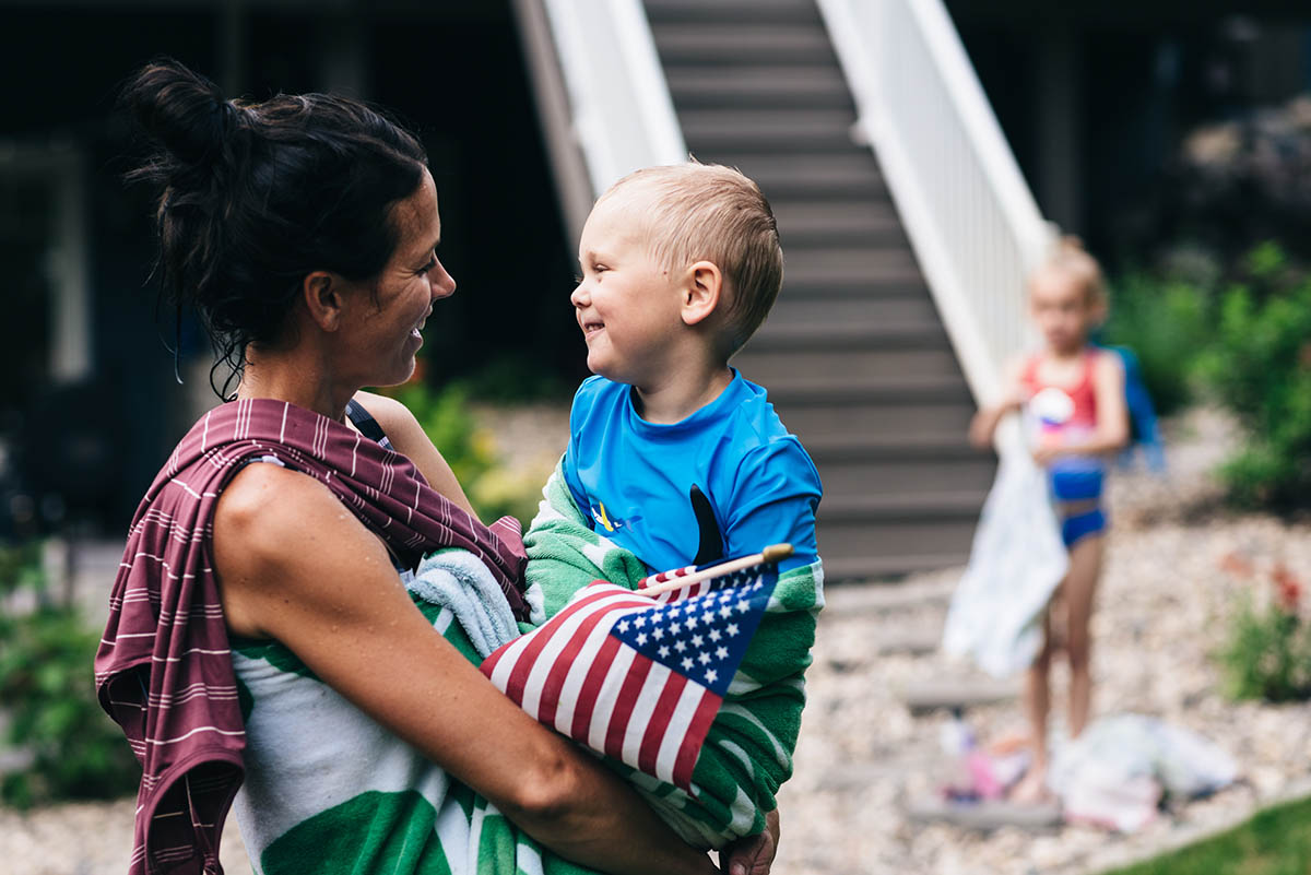 Mother holds son wrapped in beach towel smiling at him.