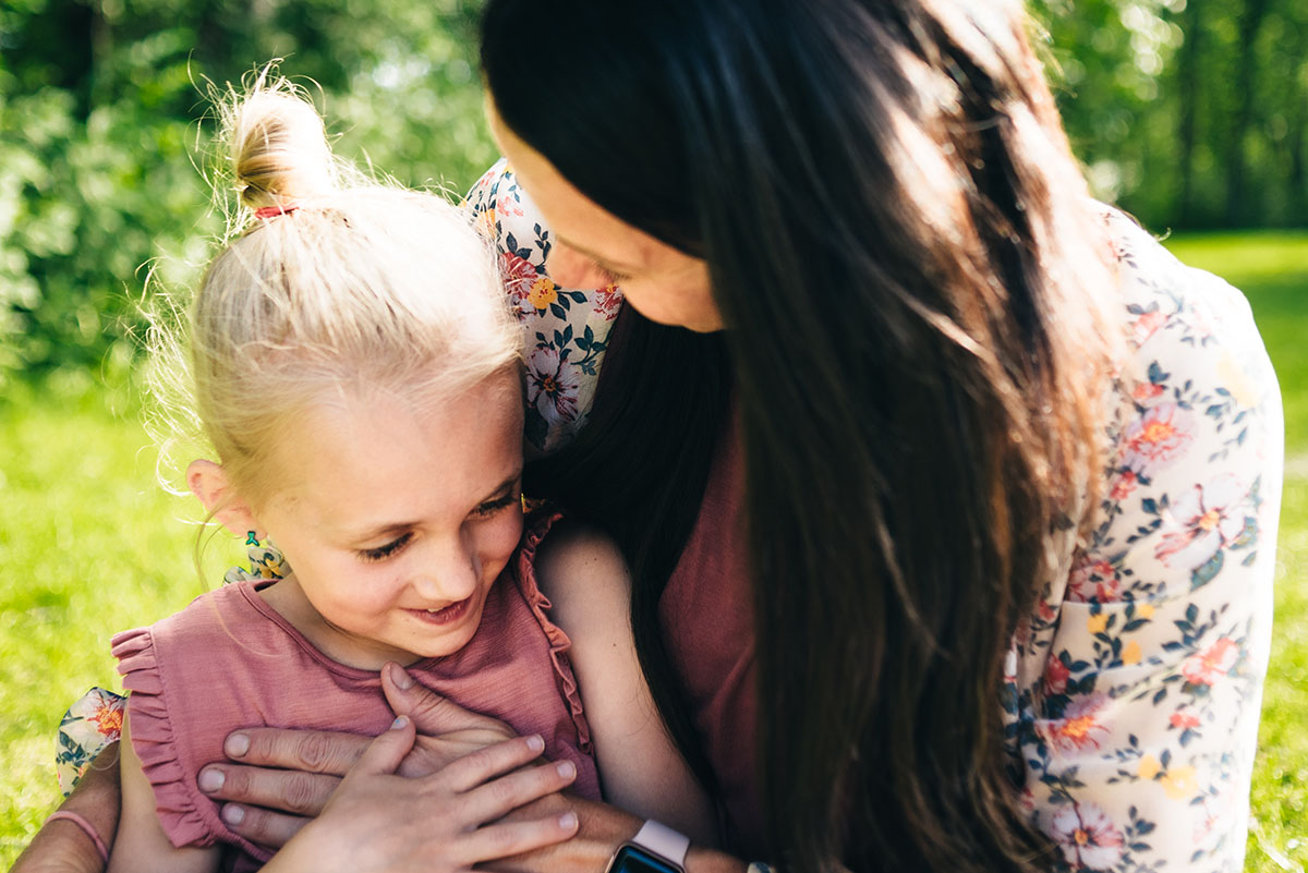 Mother with hand on daughters chest as they sit together in the grass.