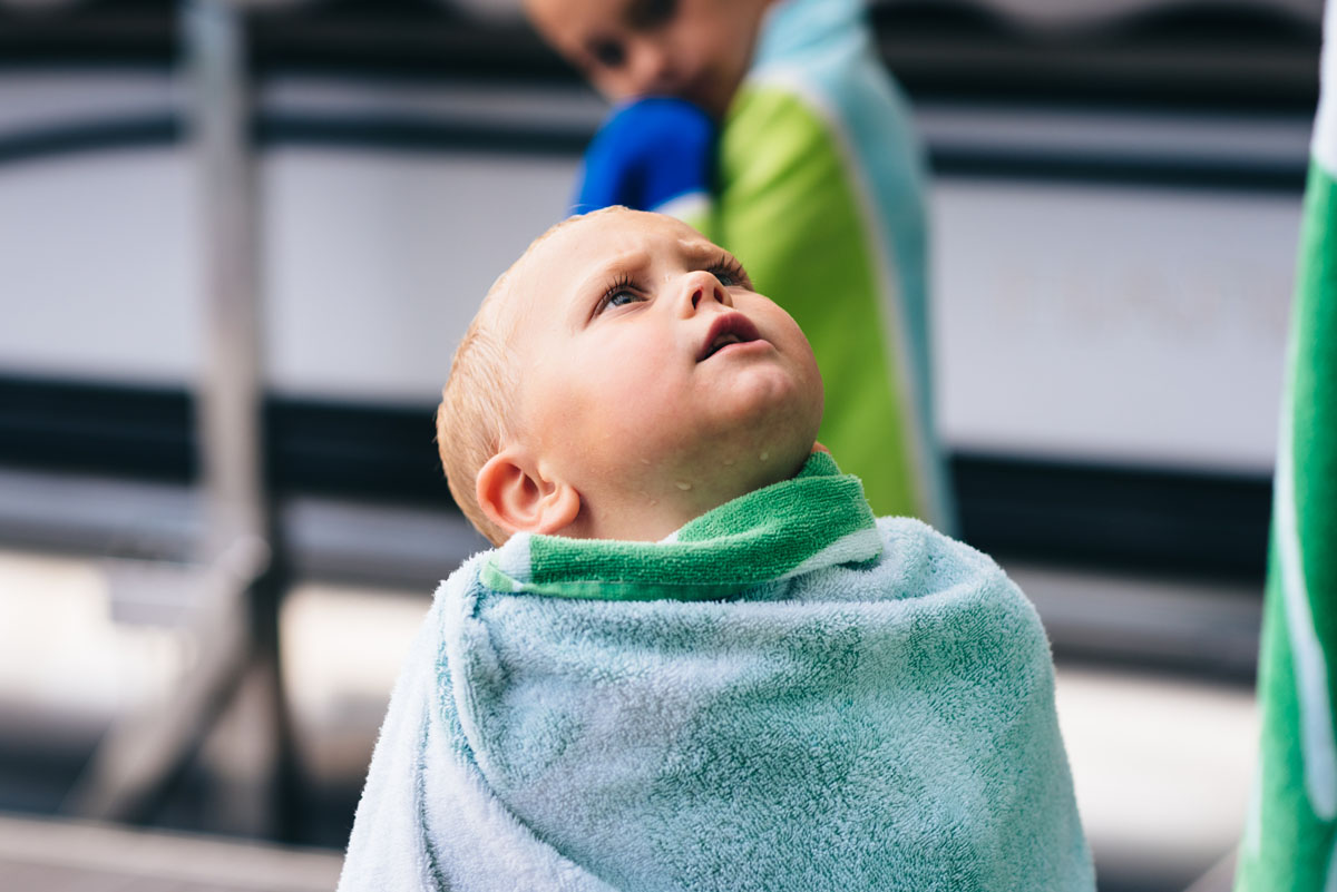 Little boy wrapped in beach towel looks up.