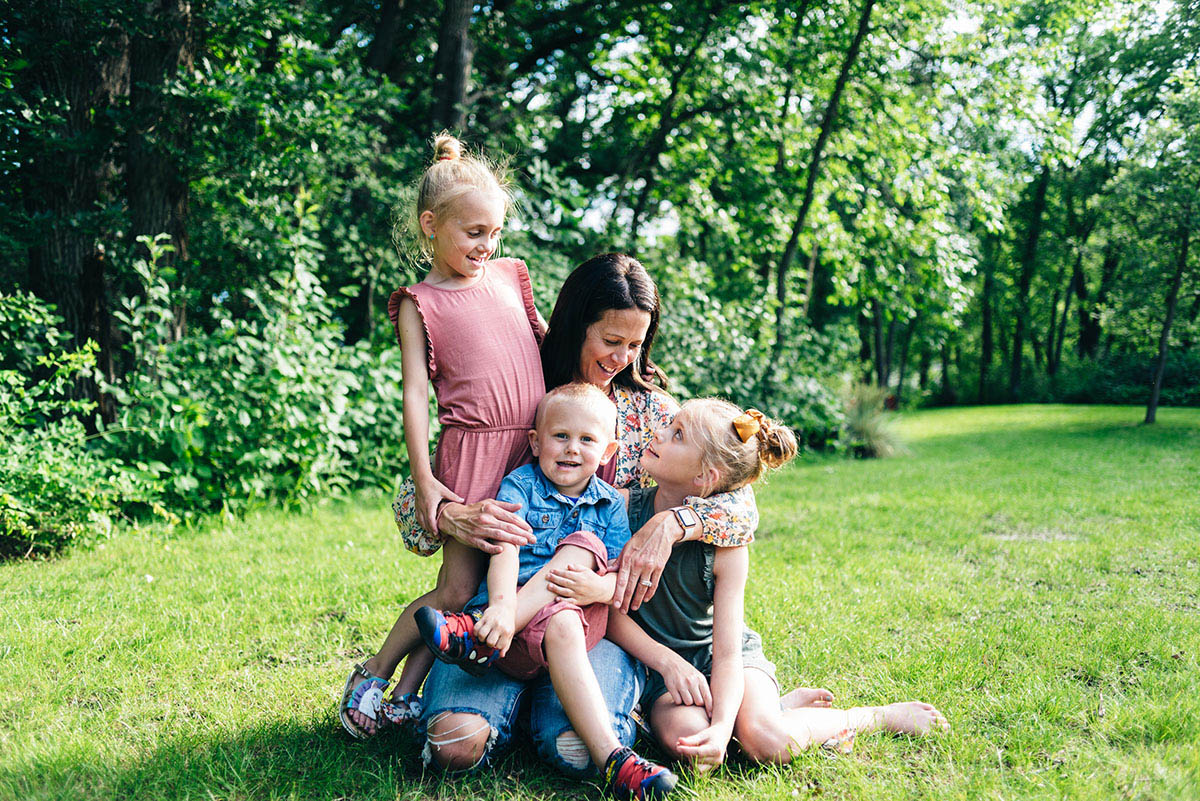 Mother sitting in grass surrounded by her three children.