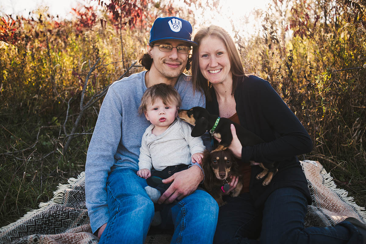 Mother, father and baby sit in tall grass during sunset session.