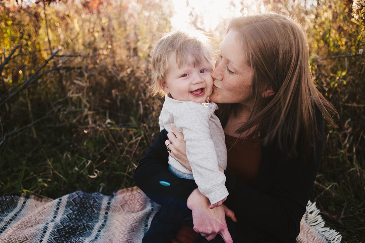 Mother kisses son as he smiles at the camera during a sunset family session in Plymouth, MN.