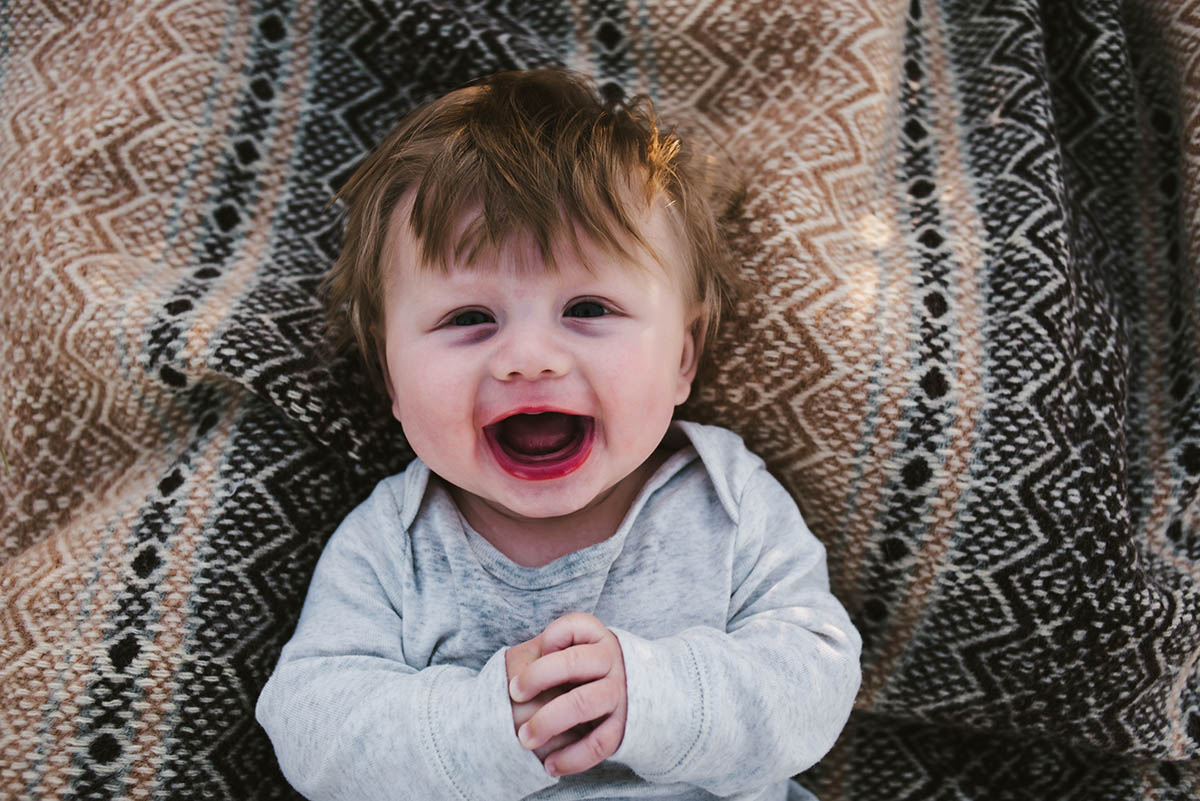 Toddler smiles as he lays on blanket.