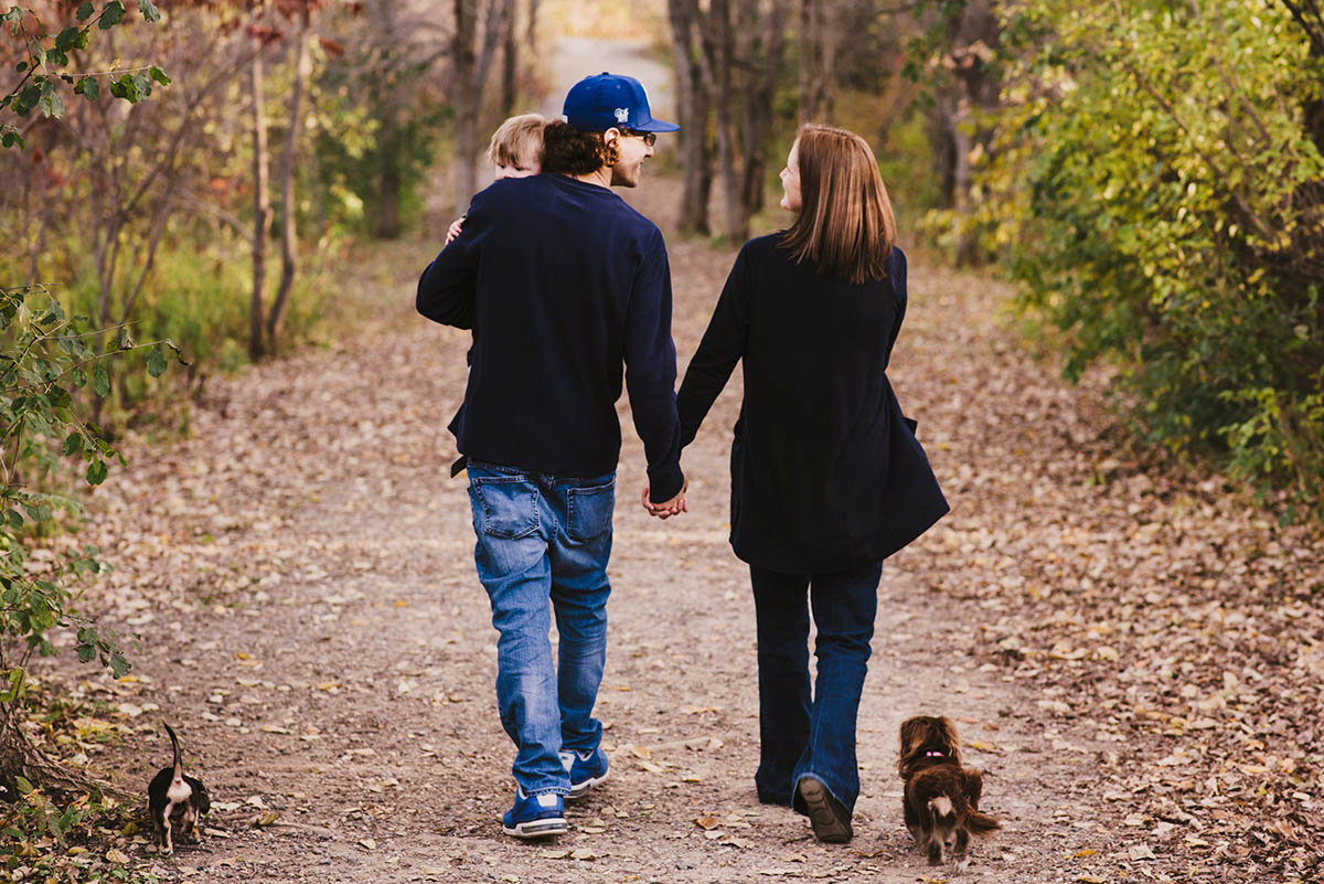 Couple holds hands and walks away from camera while dachshund dogs trot beside them.