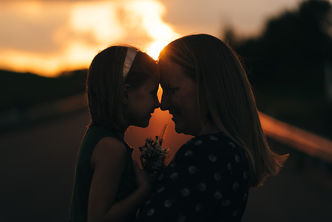 Mother and daughter silhouette in sunset. Touching noses.