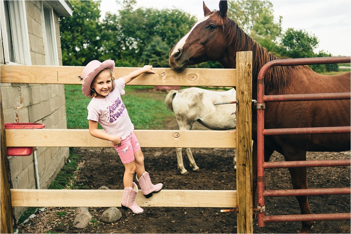 Girl climbs fence while horse looks on.