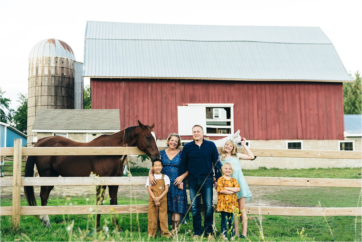 Family stands near horses with barn in the background.