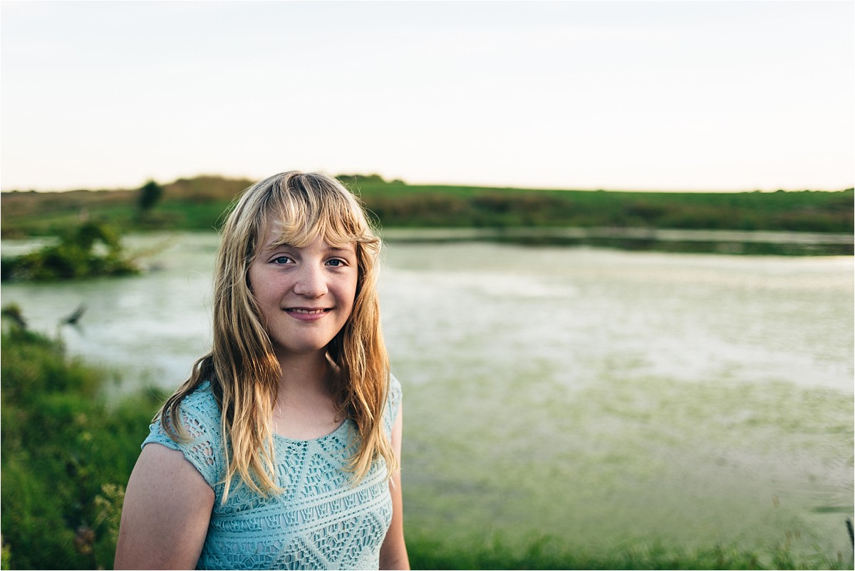 Teenage girl stands near pond and smiles at camera.