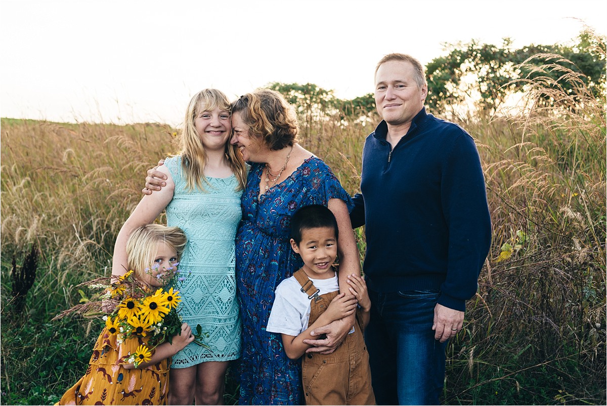 Mother and father hug kids as they pose for photo in a field.